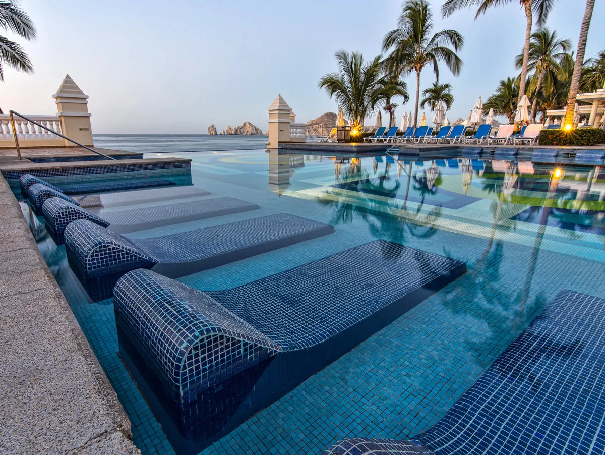Blue-tiled resort pool in Cabo San Lucas, with a view of Land's End and the Arch in the distance