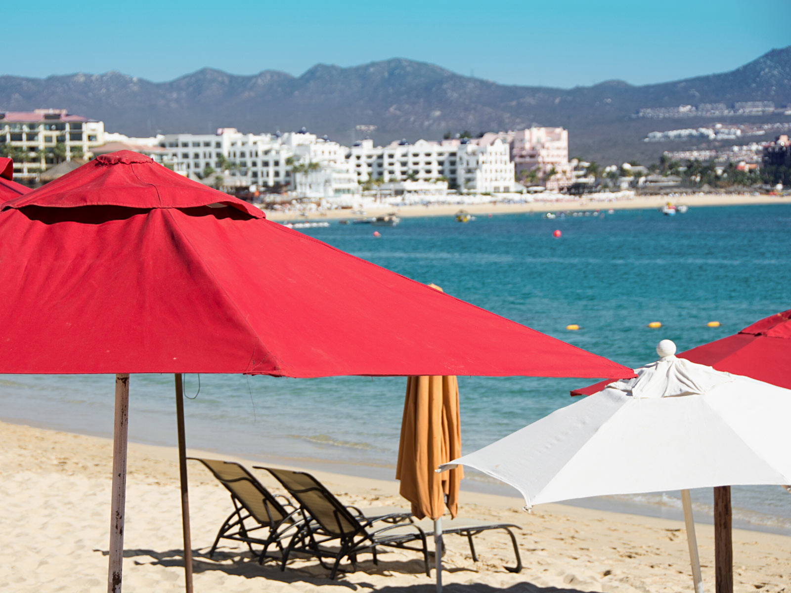 Red umbrellas by beach chairs on Medano Beach in Cabo San Lucas