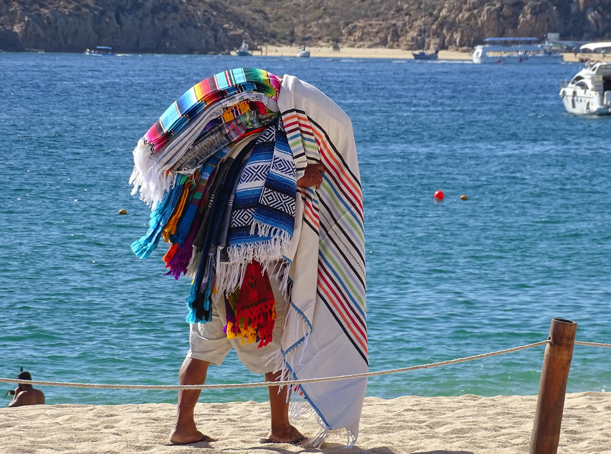 A beach vendor in Cabo San Lucas, laden down with Mexican blankets