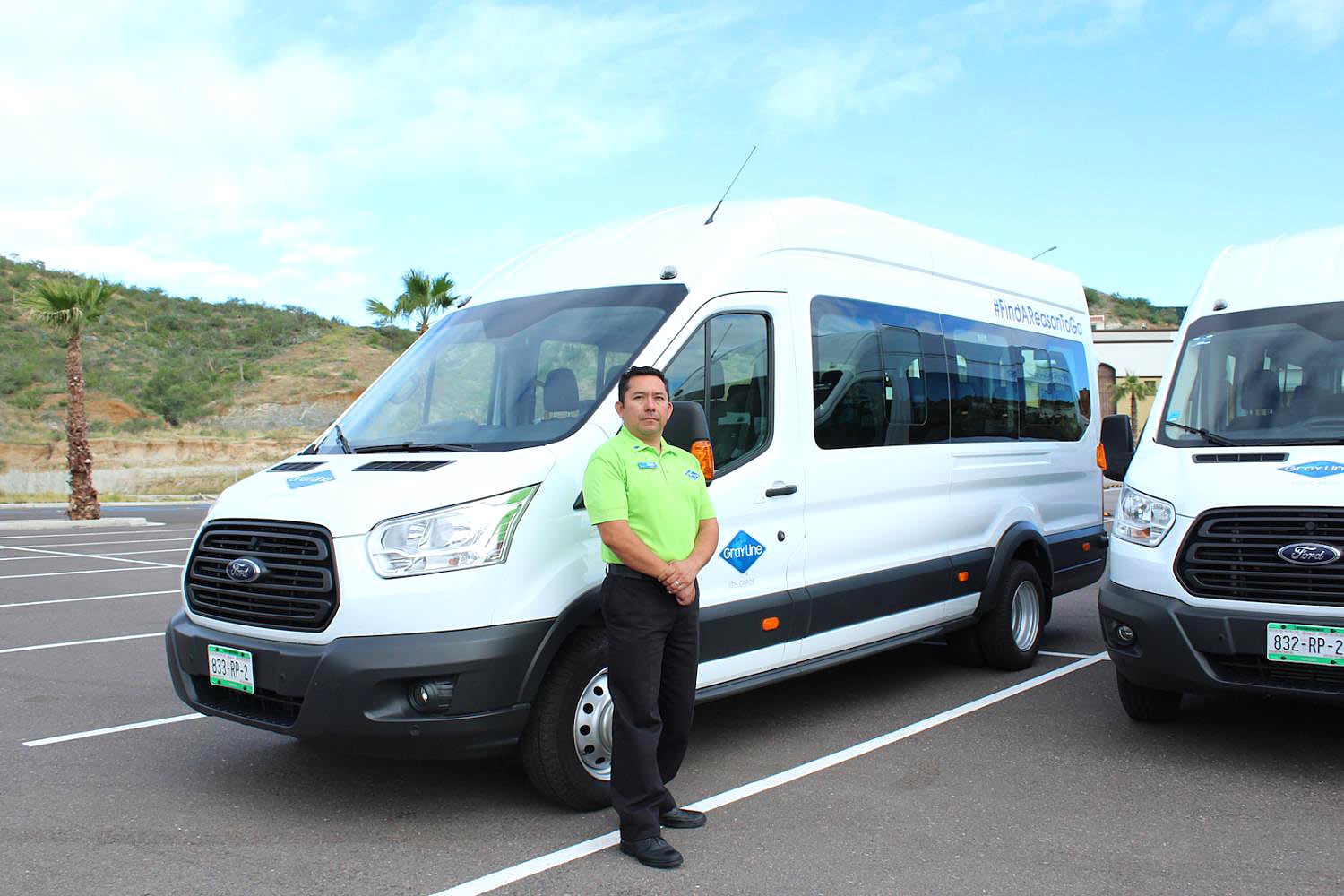 Gray Line Los Cabos driver in lime green shirt and black pants, standing beside white Gray Line van