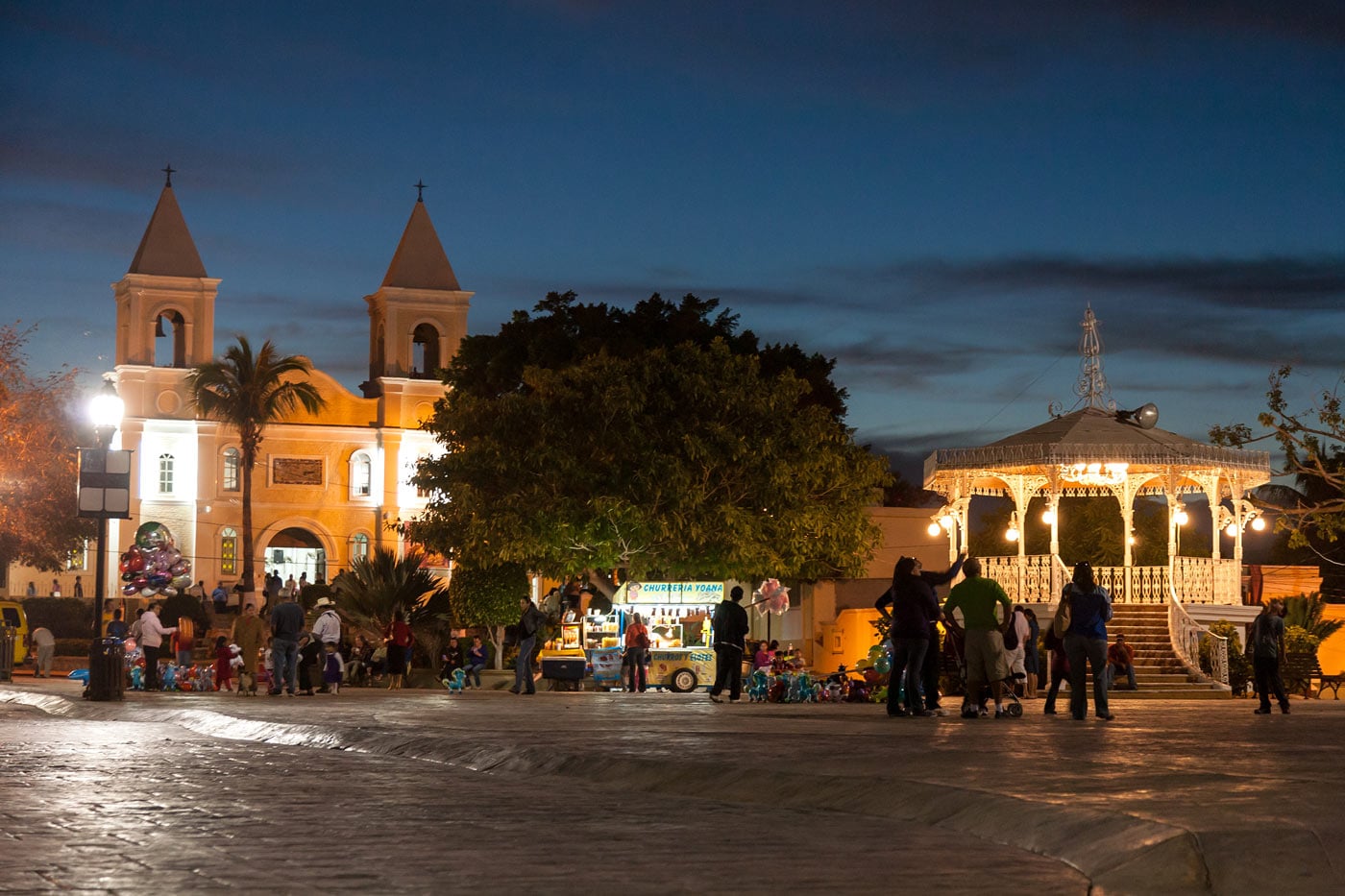 San Jose del Cabo Mission and town square illuminated at night, with people gathered around the plaza