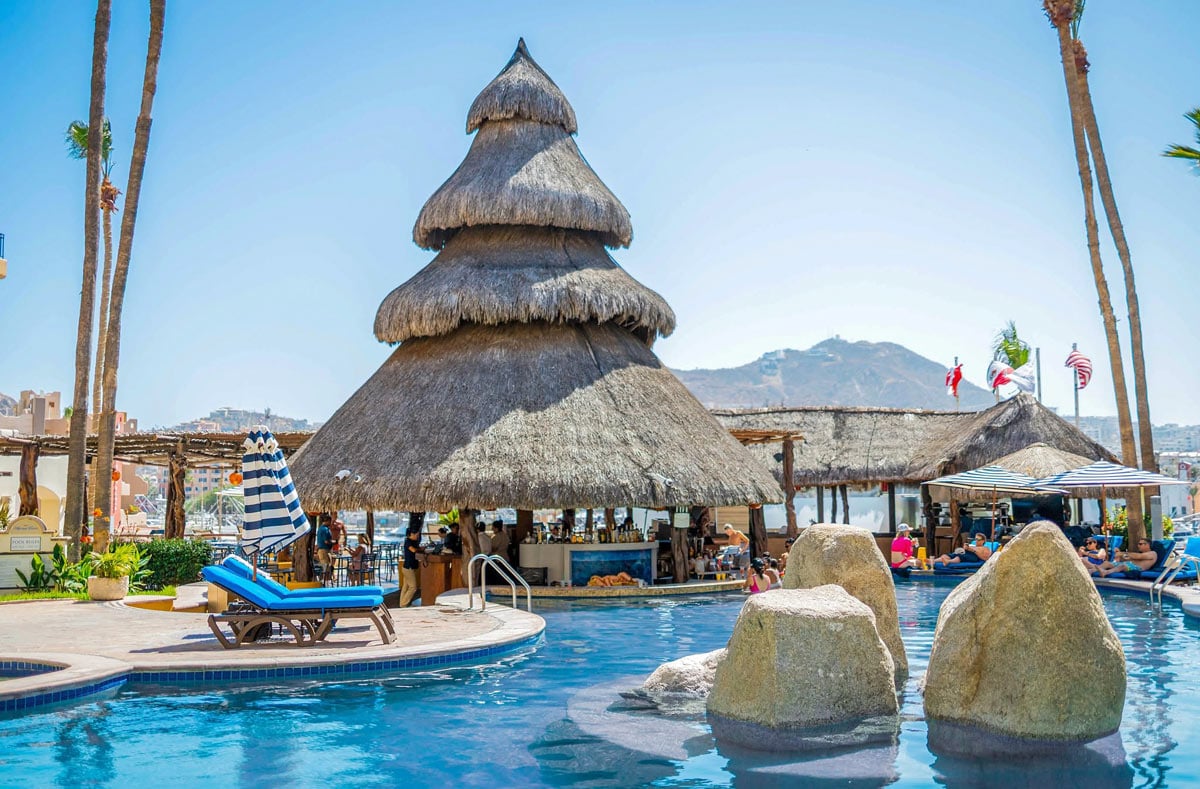 Blue cushioned loungers and thatched palapa pool bar at Marina Fiesta Resort & Spa in Cabo San Lucas