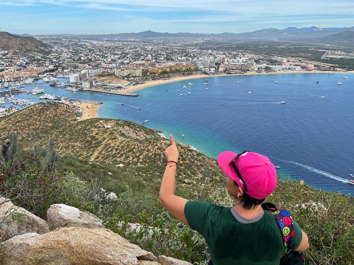 Young woman in pink cap looking at views of Cabo San Lucas from the top of Mt. Solmar