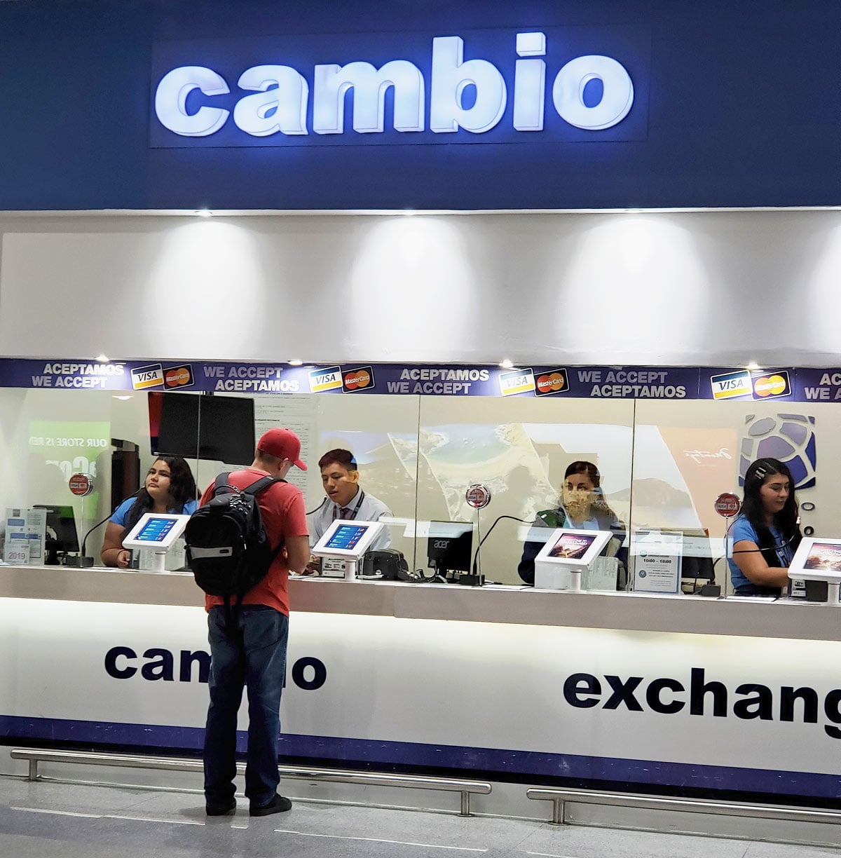 Man in red T-shirt standing by Globo Cambio currency exchange counter in the international Arrivals area at Los Cabos Airport (SJD)