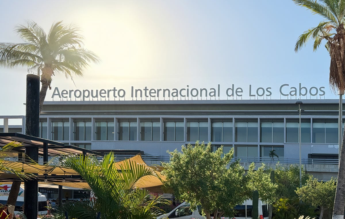 Exterior of Los Cabos International Airport (SJD) with palm trees and the airport sign under blue skies