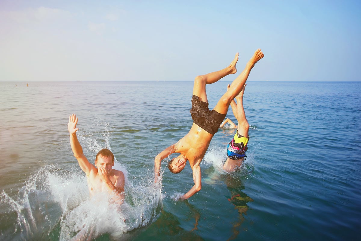 Young men jump and dive into the sea from a boat.